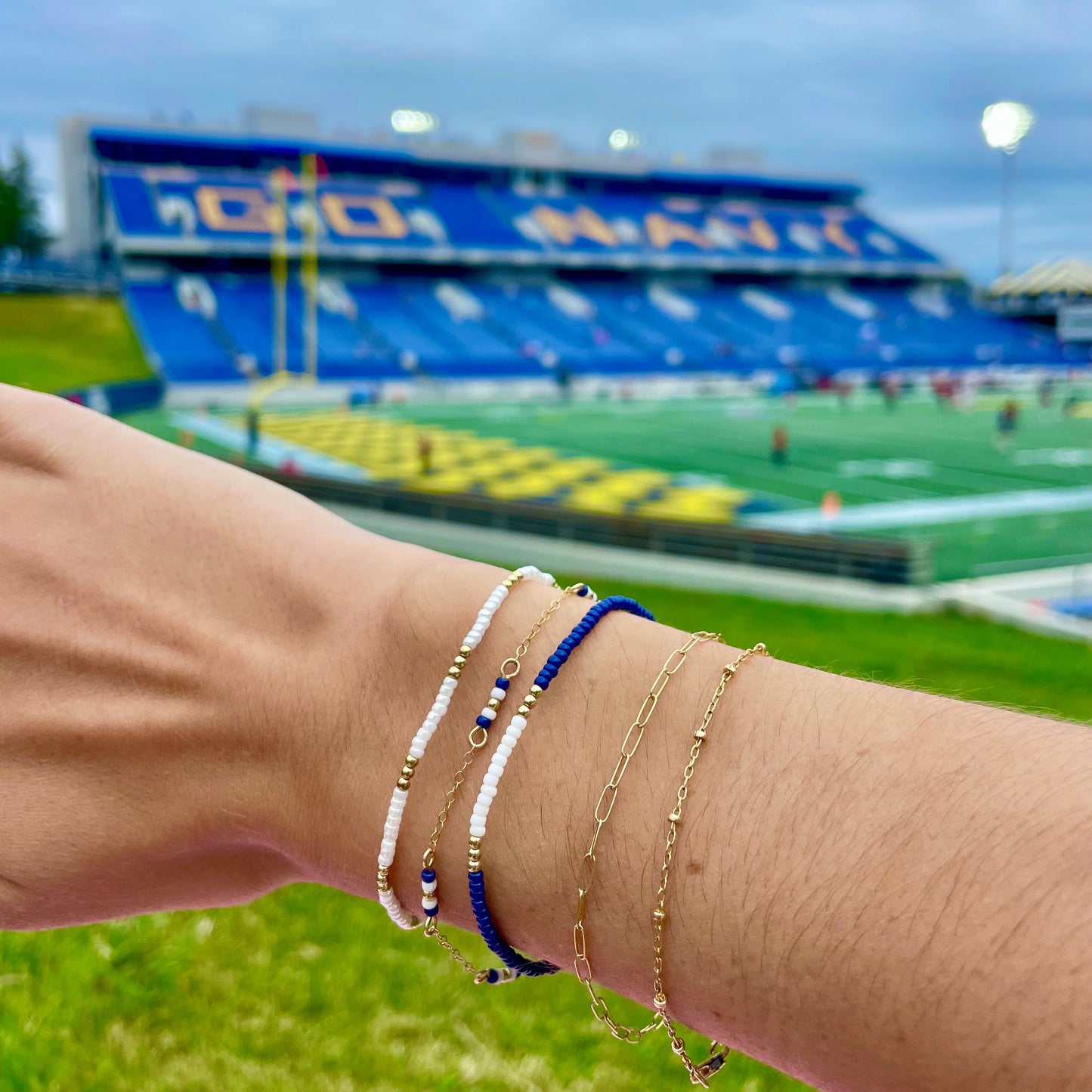 Person wearing multiple bracelets on a wrist with a blurred stadium background