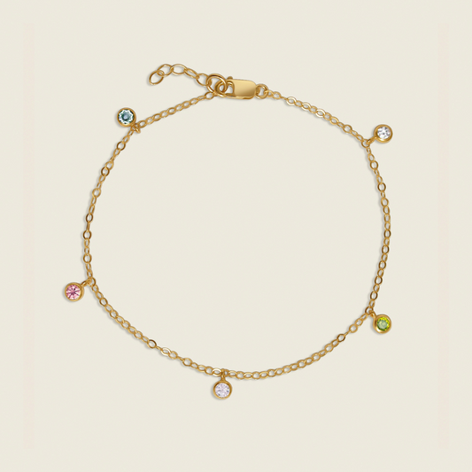 A gold-filled bracelet with multiple colored gemstone charms, including clear, amethyst, peridot, pink, and sapphire, displayed against a white background.