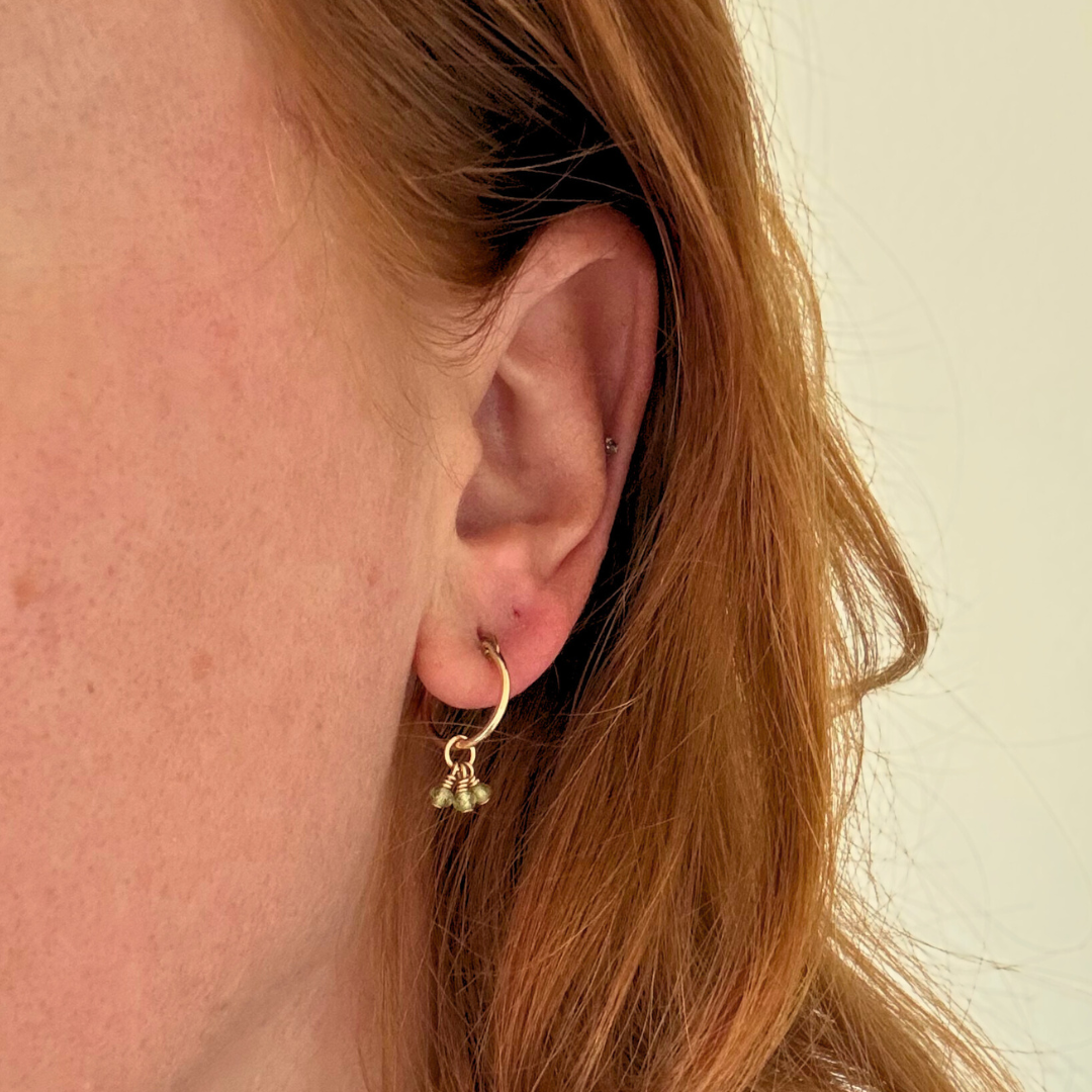 Gold hoop earring worn by a person with red hair against a neutral background