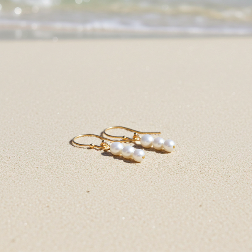 Pearl earrings on a sandy beach with ocean waves in the background