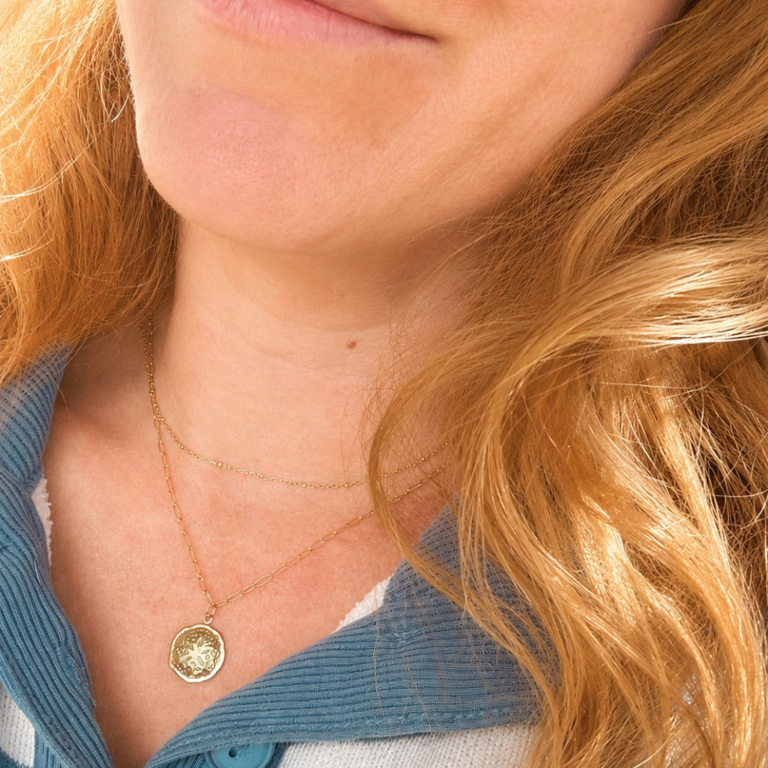 Close-up of a person wearing a gold paperclip necklace with a sand dollar pendant.