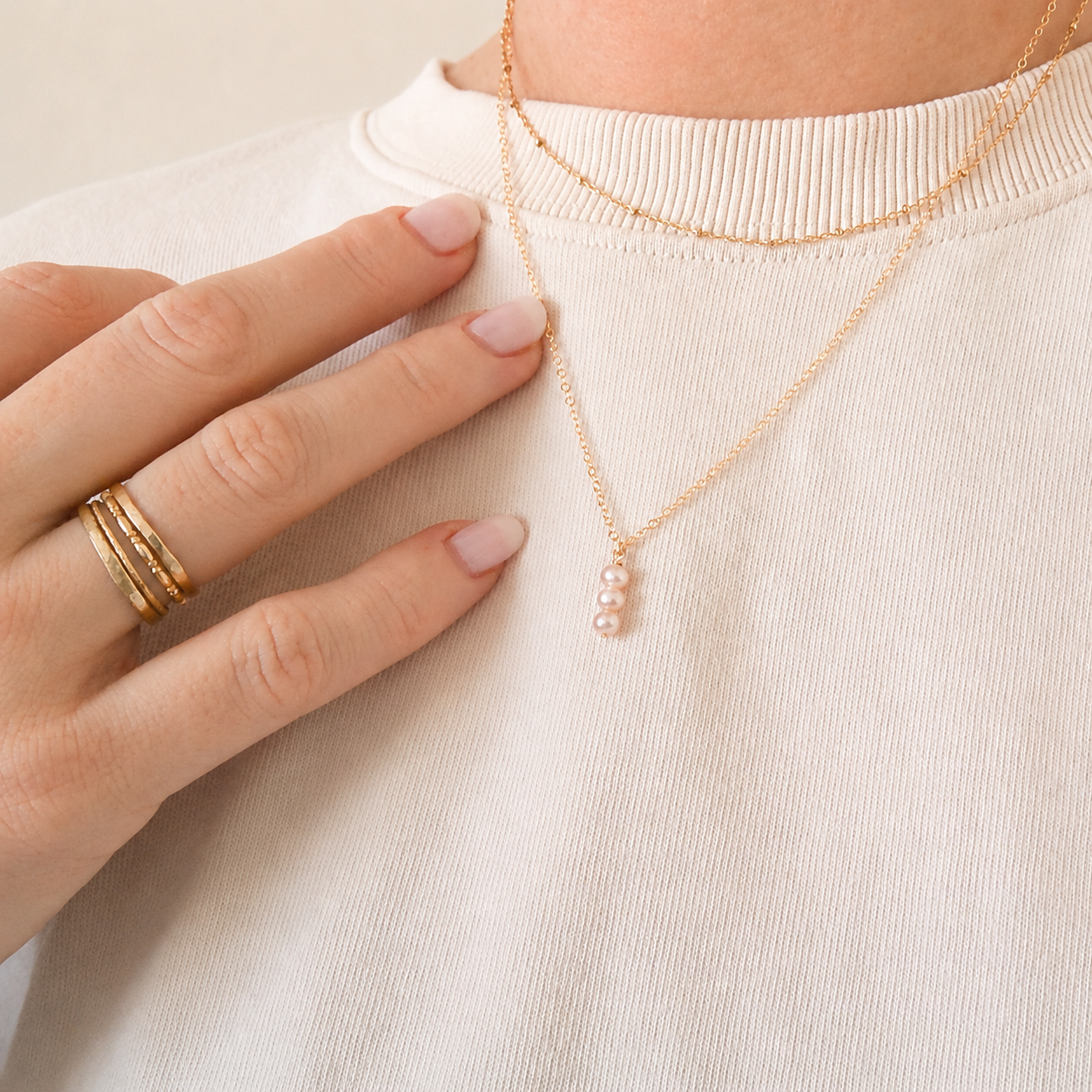 Person wearing a delicate gold necklace with a small pendant on a light background