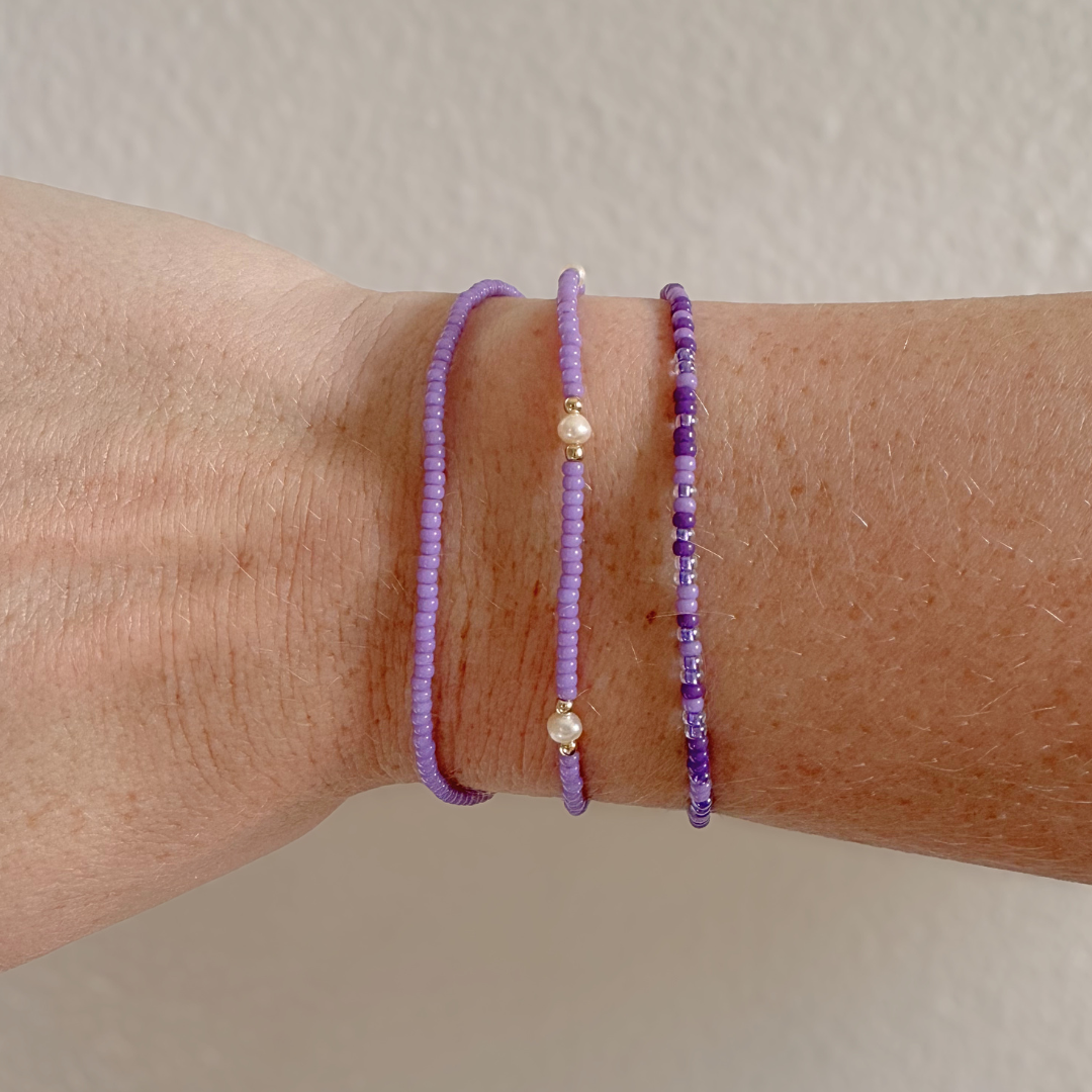 three purple beaded bracelets with gold accents on a wrist against a neutral background