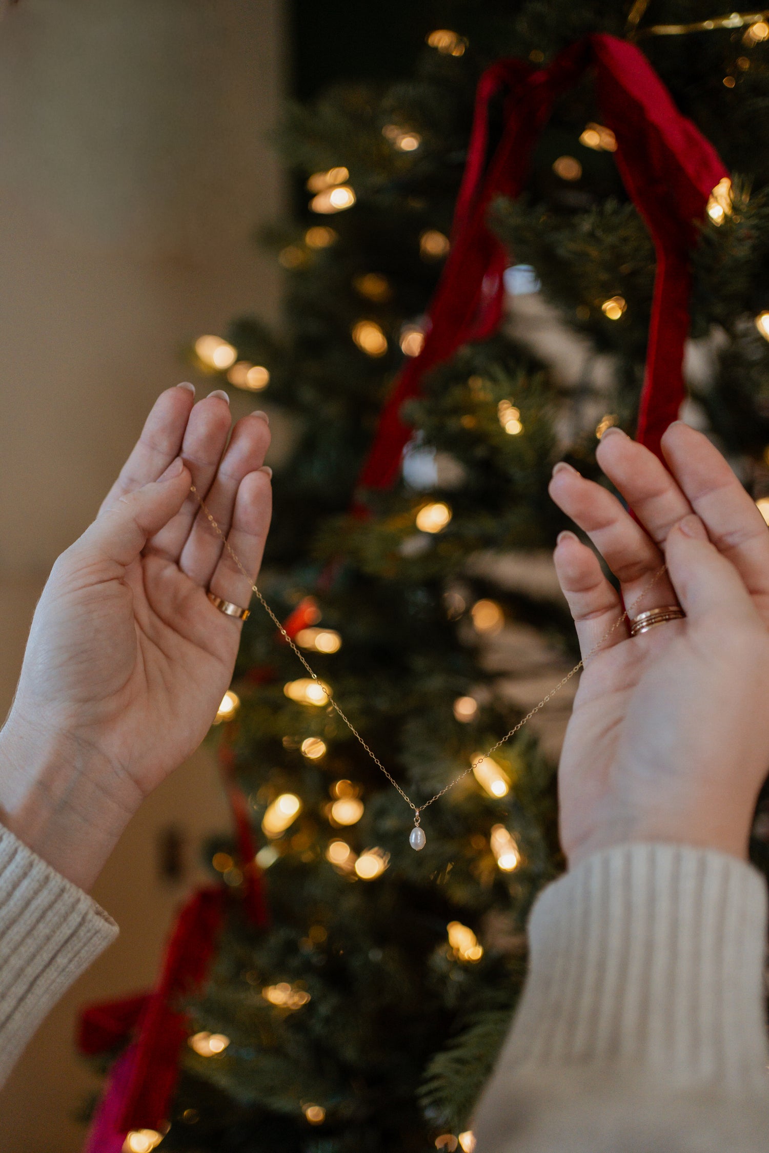 Two hands holding a red ribbon in front of a decorated Christmas tree.