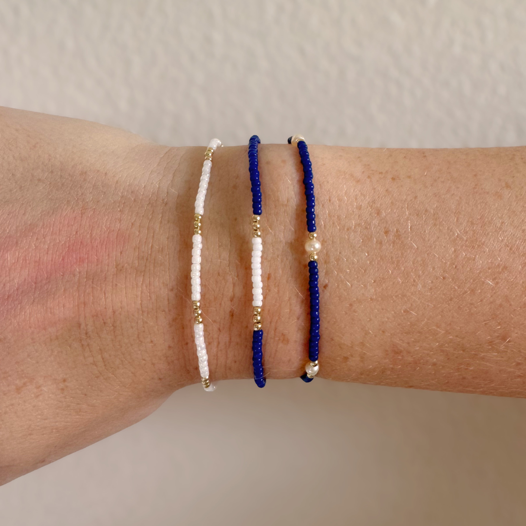 Three beaded bracelets on a wrist against a plain background
