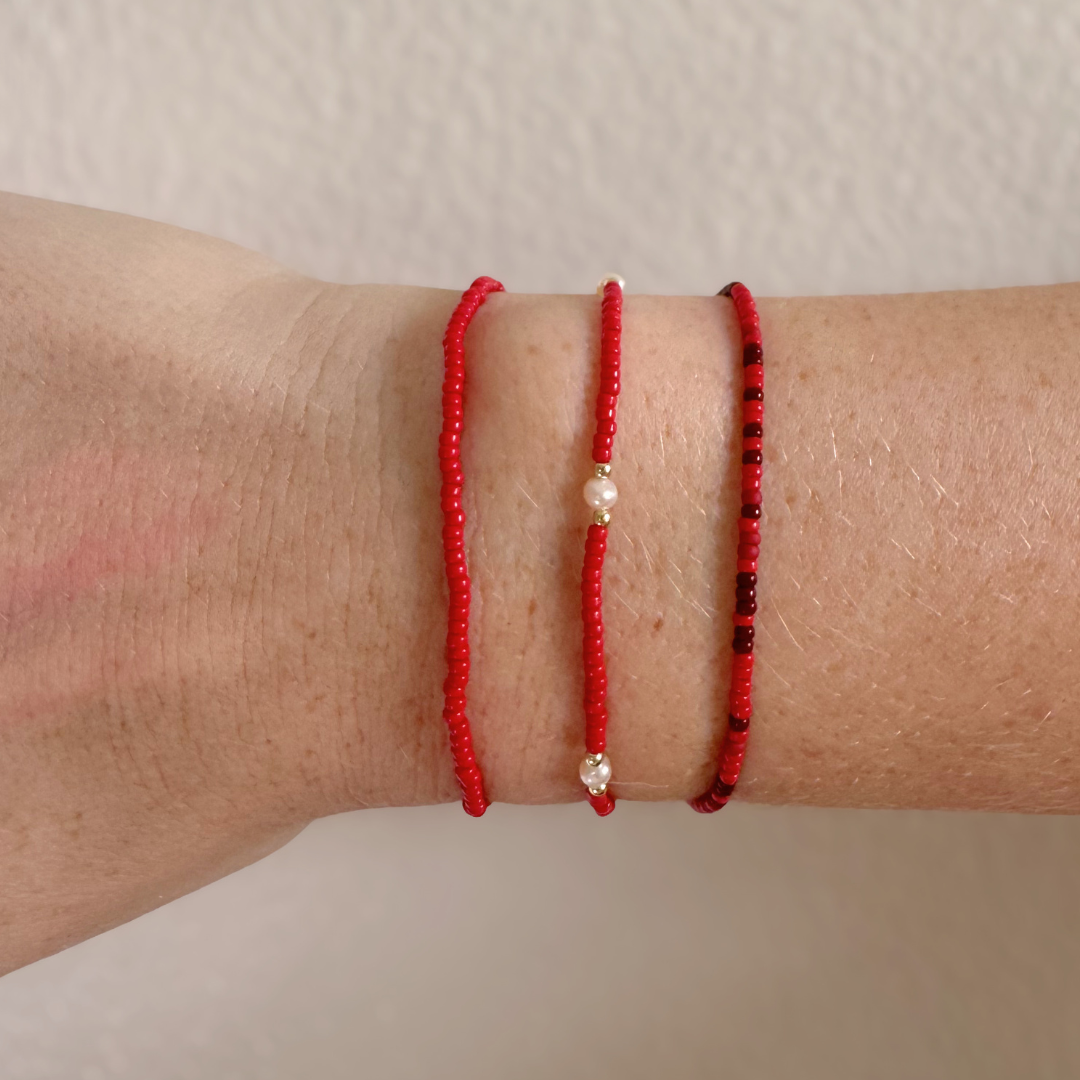Three red bracelets with small beads on a wrist against a neutral background