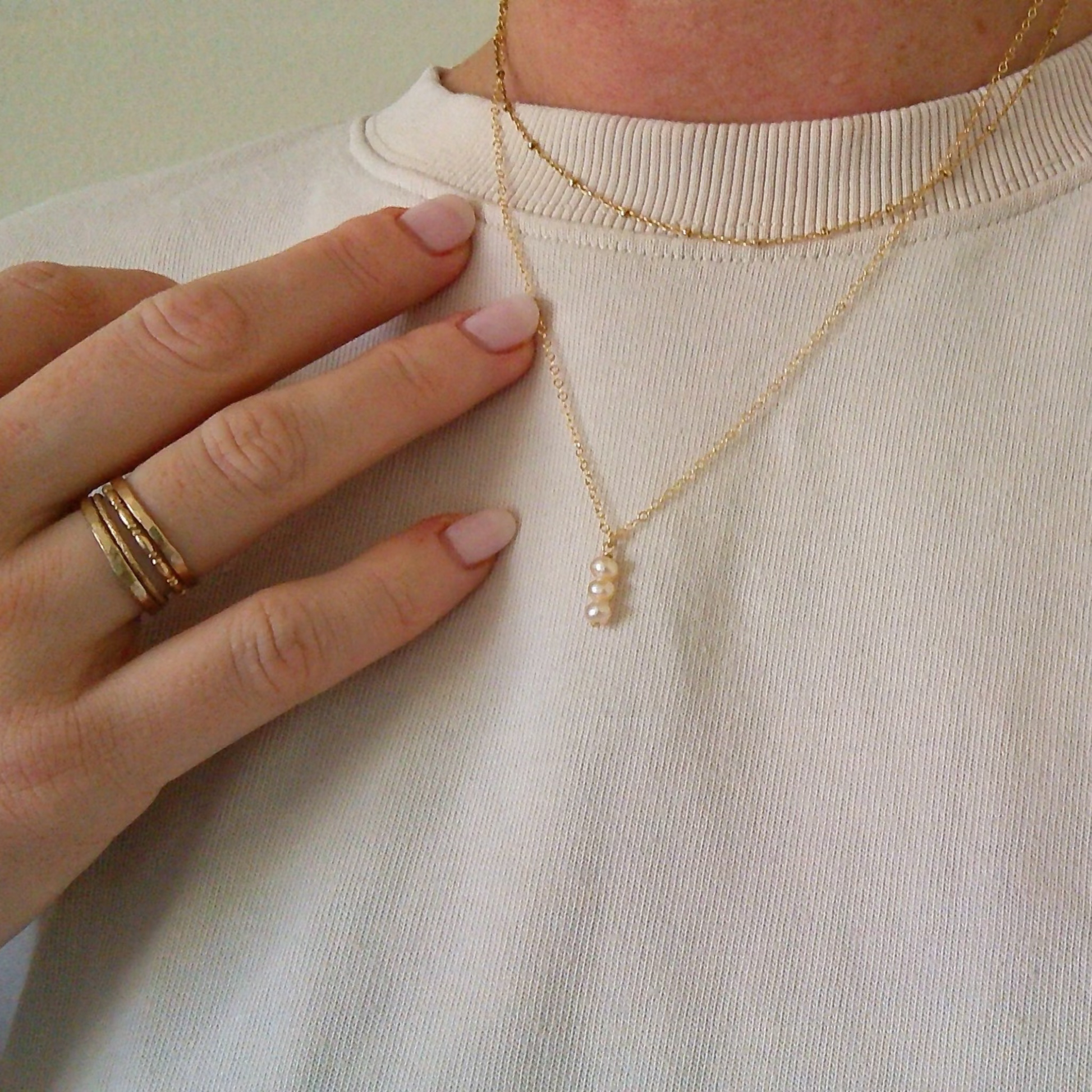 Person wearing a gold necklace with a small pendant on a plain background