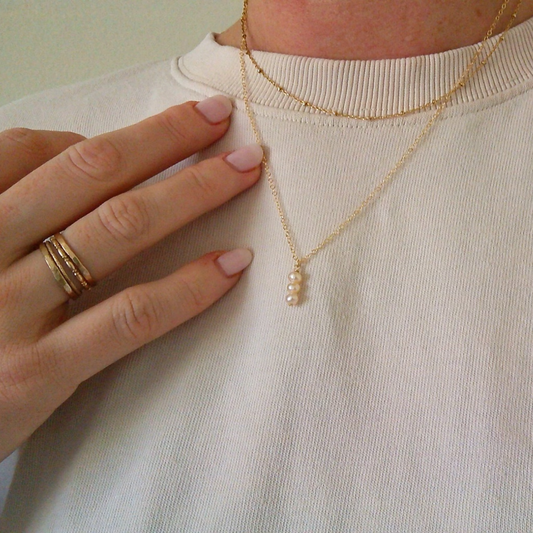 Person wearing a gold necklace with a small pendant on a plain background