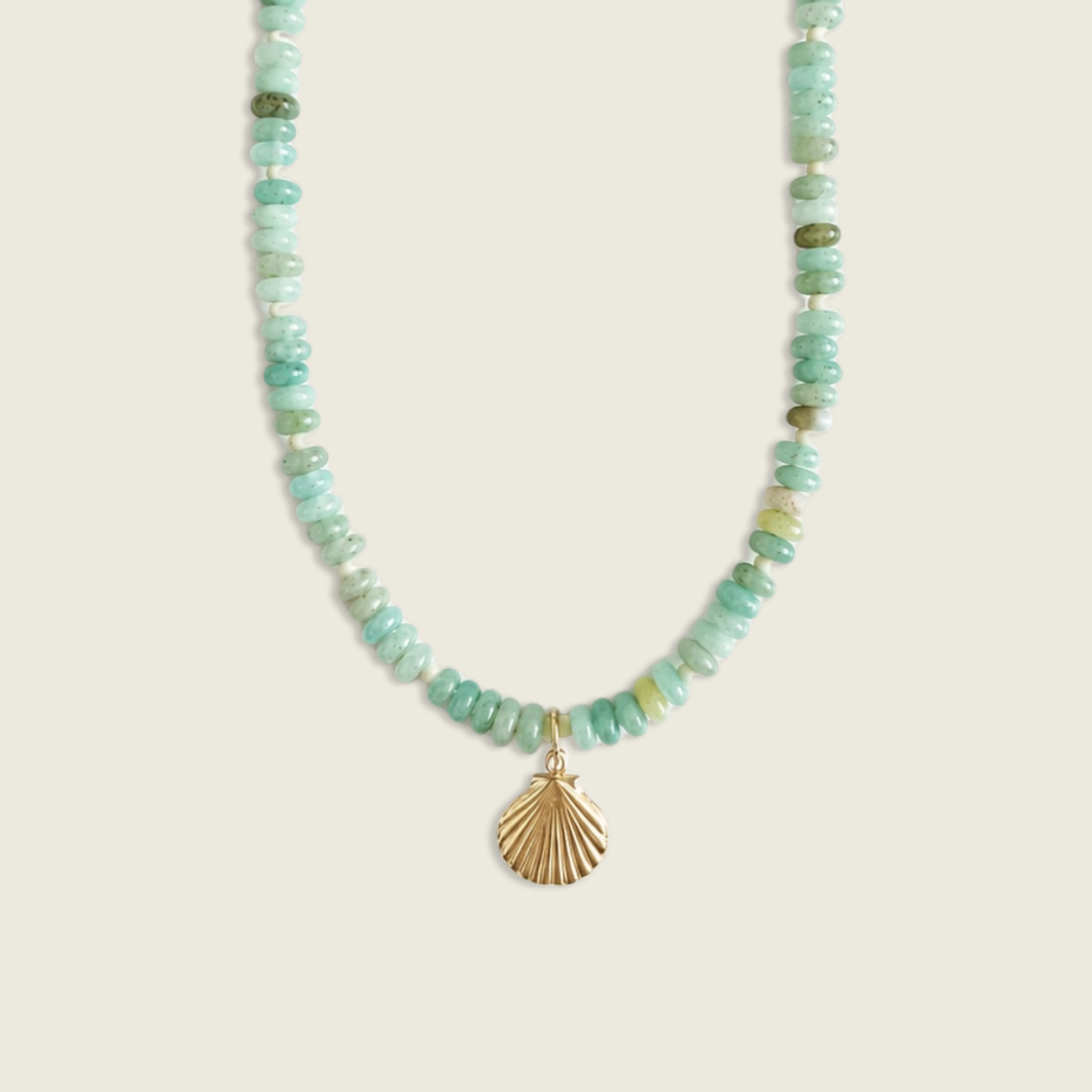 A beaded necklace featuring light green and white marbled stone beads with a gold-toned shell-shaped pendant, displayed against a solid beige background.