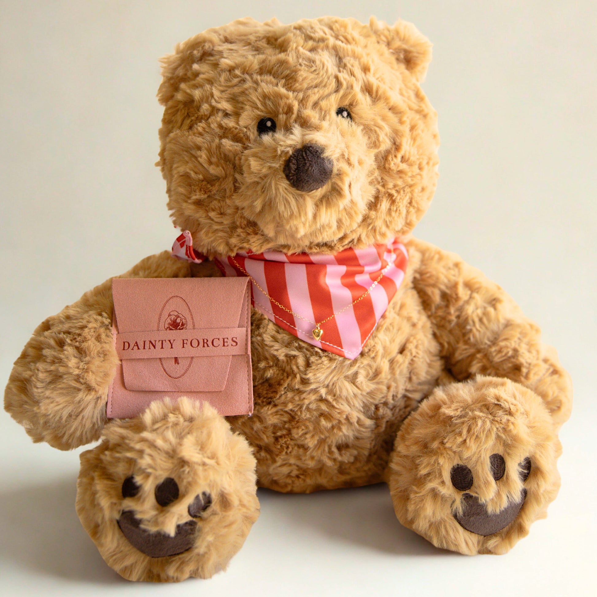 Brown teddy bear with a red and white striped scarf and a pink tag on a beige background