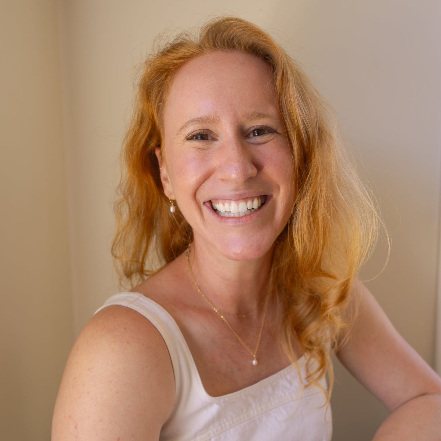 Woman with red hair wearing a white top against a beige background