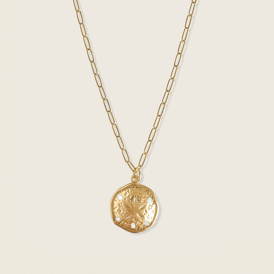 Gold necklace with a sand dollar pendant on a beige background